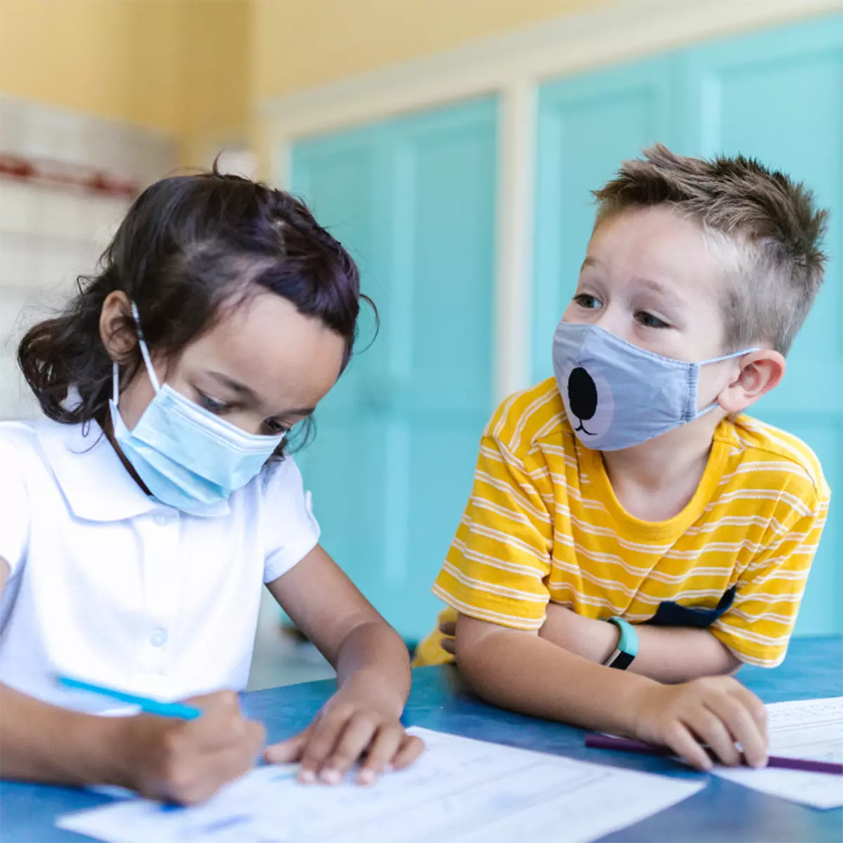Little boy and little girl with masks on coloring a piece of paper